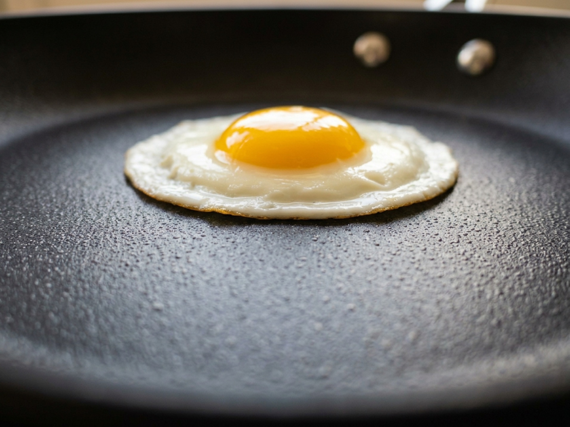 Fried egg sliding freely on dark PTFE nonstick surface showing coating texture