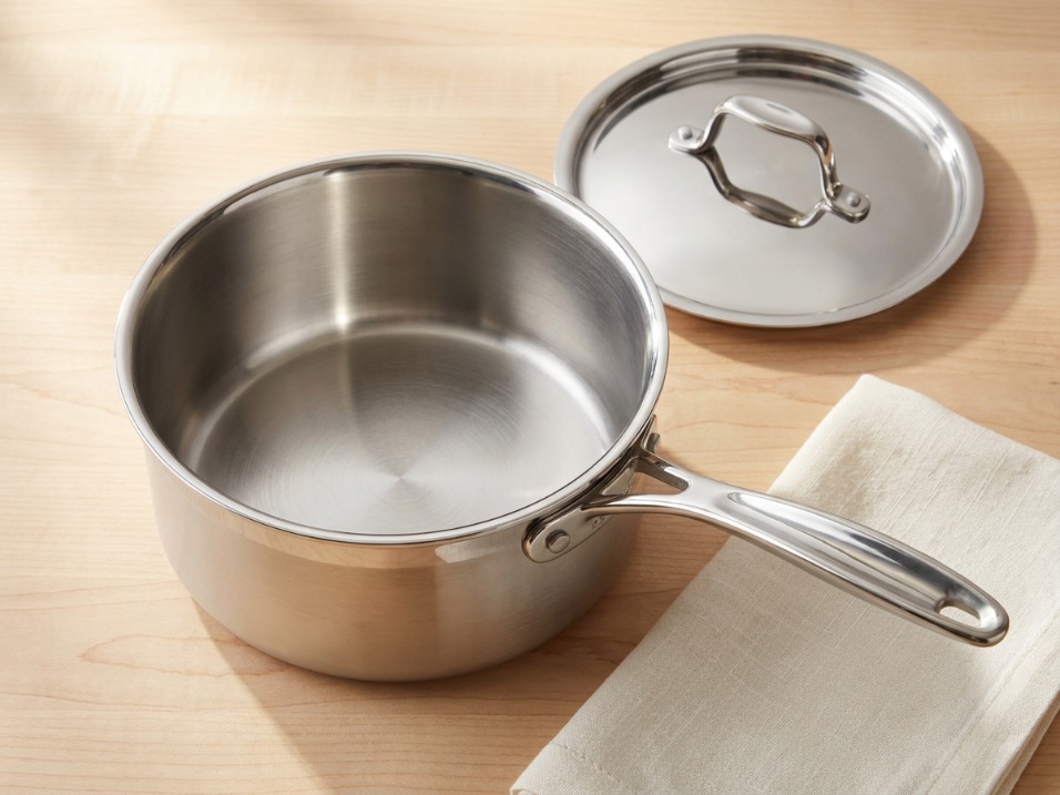 A stainless steel saucepan with polished interior and lid beside it on a maple countertop with a linen napkin