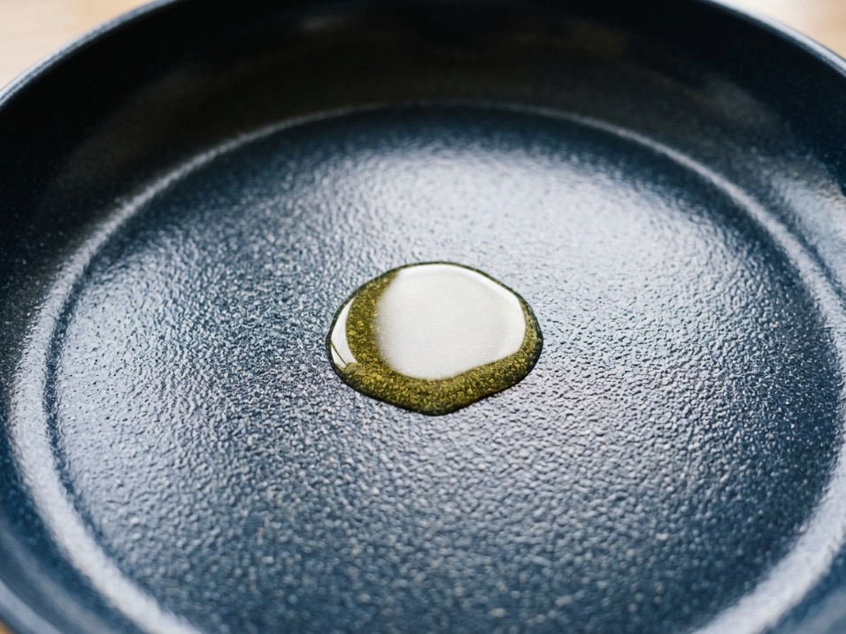 Close-up of a ceramic nonstick pan interior showing granular texture with a pool of olive oil beading on the surface