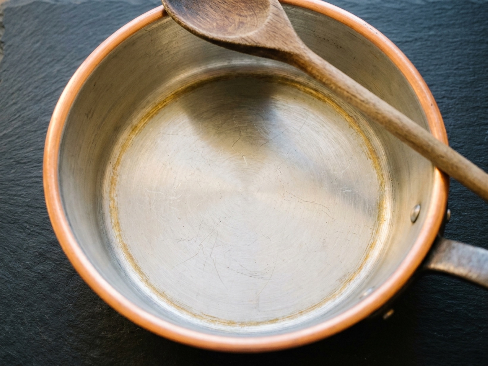 Tin-lined copper saucepan interior with use marks and golden patina at edges