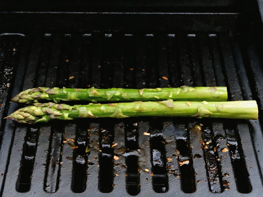 Asparagus spears resting across the ridges of a cast iron grill pan, with char and oil visible