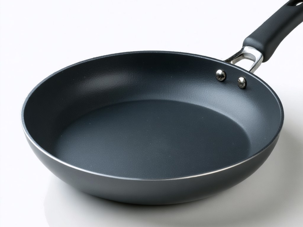 Dark hard-anodized frying pan with matte charcoal interior surface and thick reinforced walls on a white background