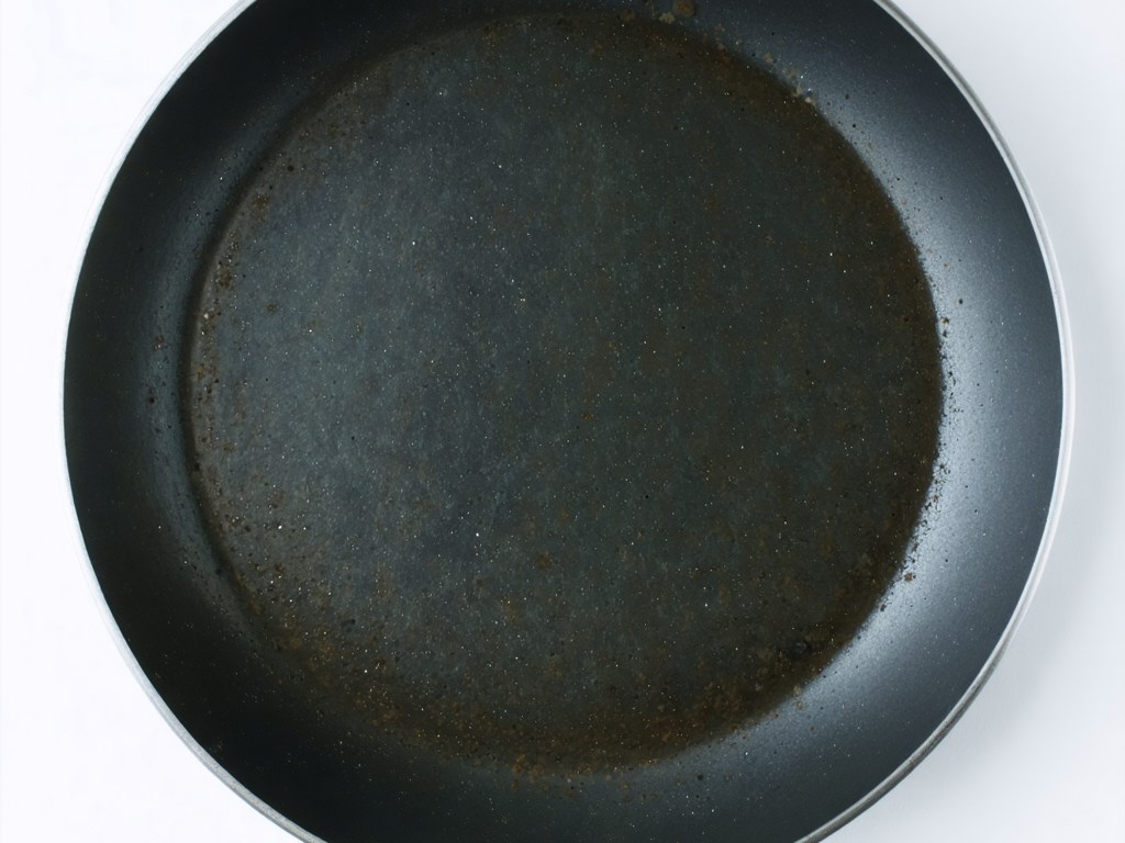 Worn nonstick frying pan with discolored coating and exposed grey patches