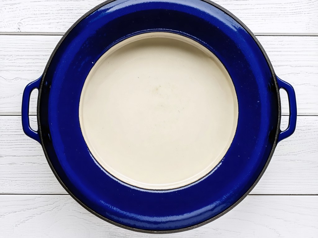 Navy blue enameled cast iron dutch oven from above on white wood, cream interior and loop handles visible