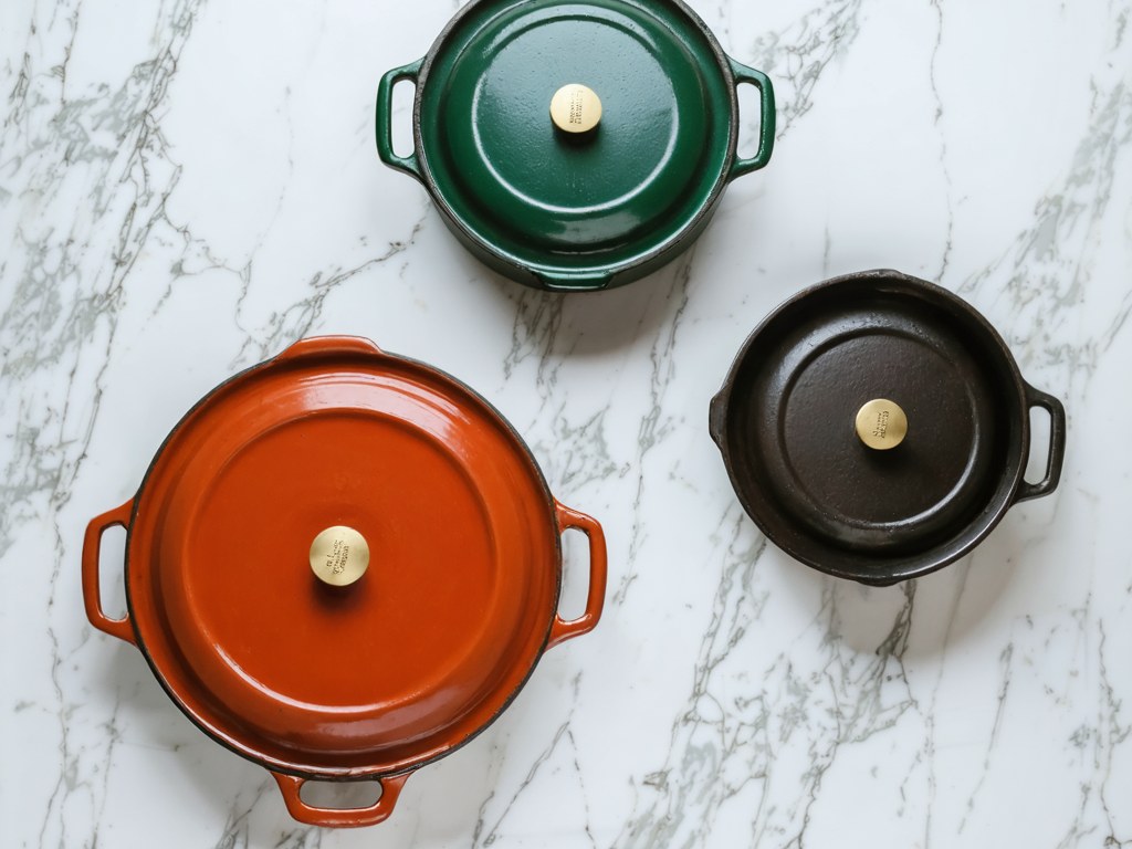 Three enameled dutch ovens in red, green, and black from large to small on marble showing size differences
