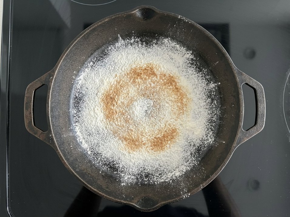 Top-down view of flour dusted in a cast iron skillet showing a toasted ring in the center from induction hot spot heating