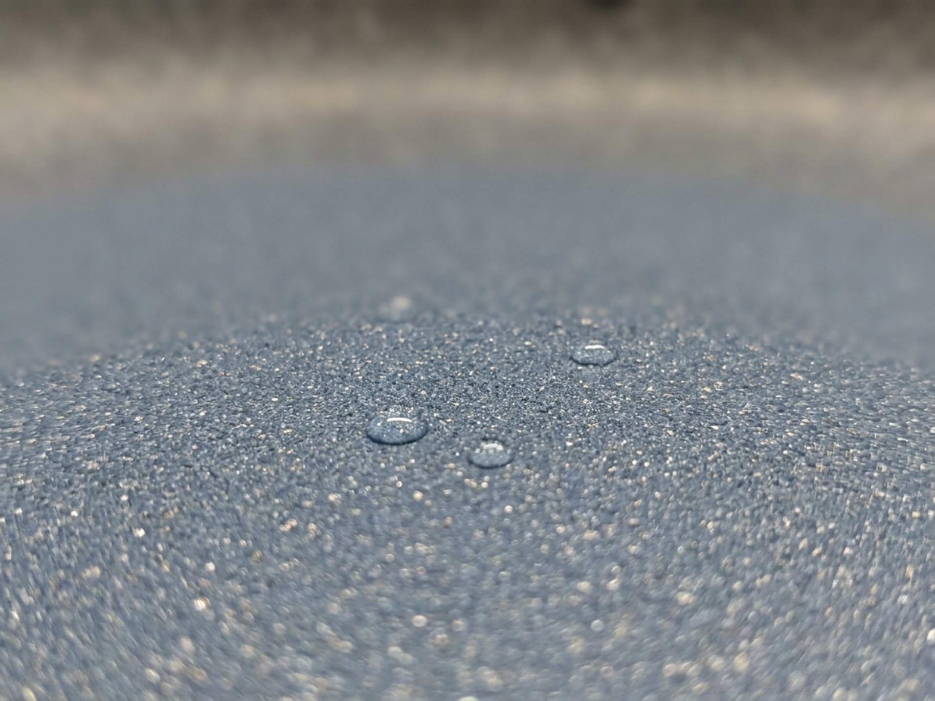 Macro close-up of ceramic nonstick coating texture with water droplets beading on the speckled surface