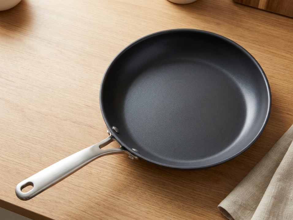 Dark matte carbon steel frying pan with a rounded handle resting on a wood counter