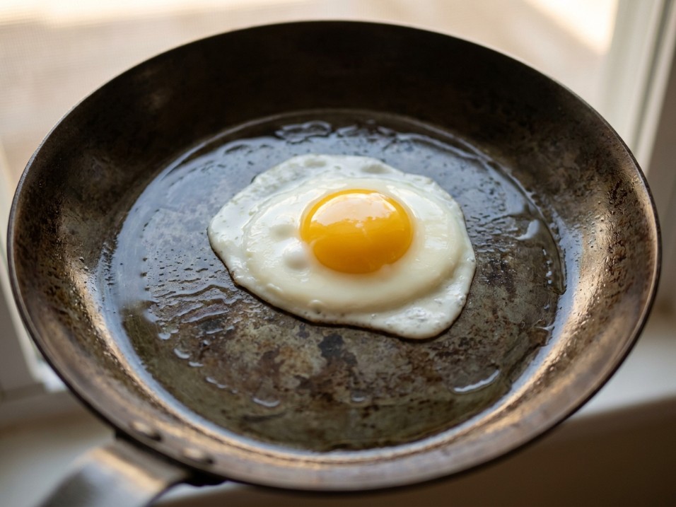 Fried egg with a set white and runny yolk sliding freely on a well-seasoned carbon steel pan with visible uneven patina