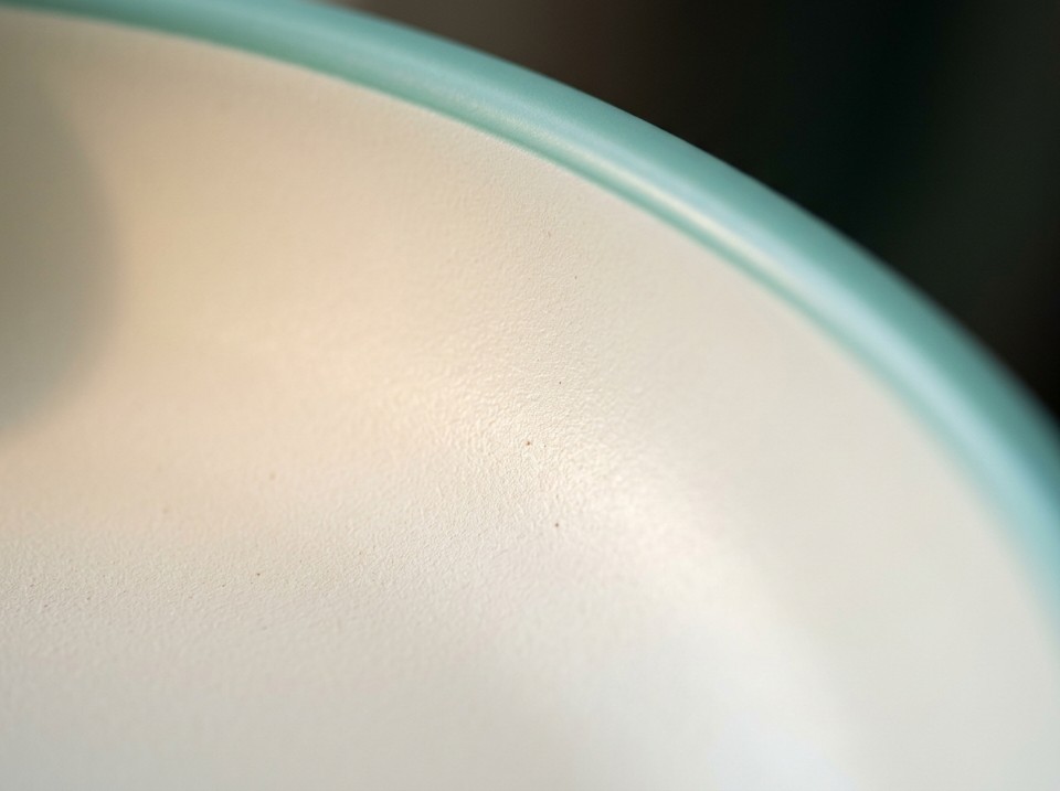 Close-up macro of a smooth cream ceramic non-stick coating surface next to a teal rolled rim edge