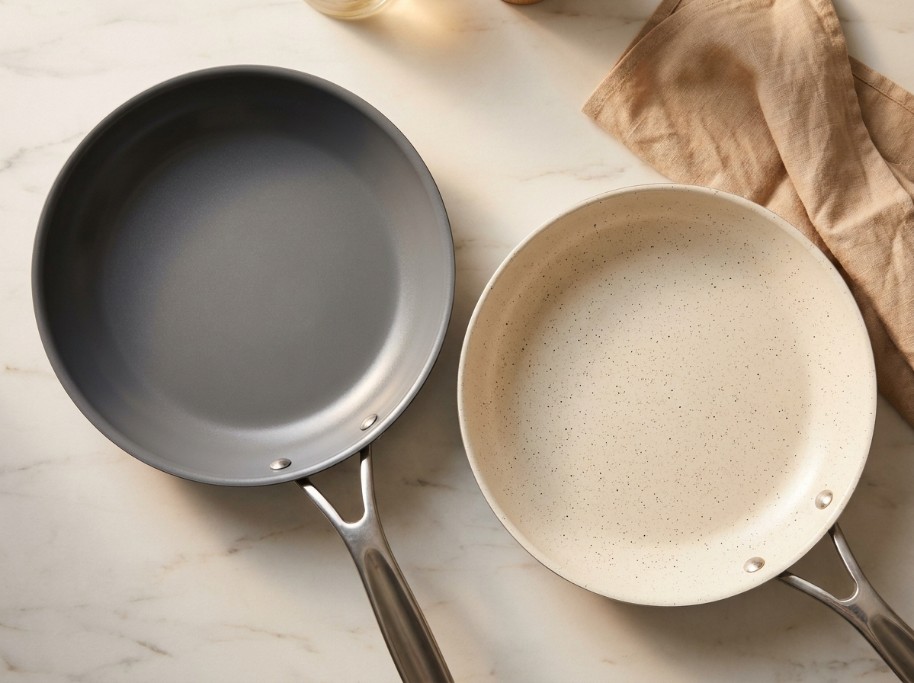 Dark matte PTFE nonstick pan and speckled ceramic nonstick pan side by side on a marble countertop